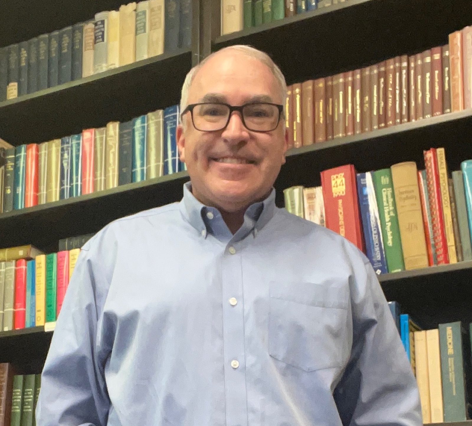 Joseph Robson, LMHC, in his office in front of a wall of psychology texts